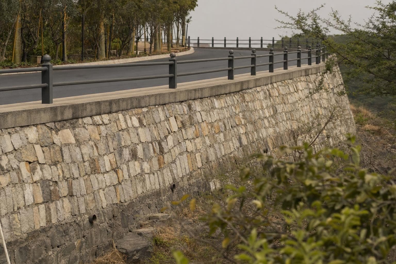 Coursed stone masonry retaining wall along a municipal road embankment